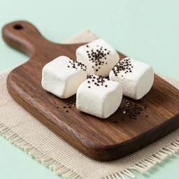 photograph of a marshmallow cube with sprinkles and chocolate flakes on a dark wooden chopping board, light green pastel, hessian cloth, styled food photography, photorealistic, 4 k