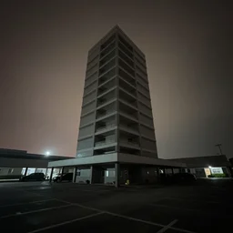 a liminal parking tower seen from inside. Low camera angle. Nighttime. Diffused light, misty atmosphere. Long shadows gives an eerie feeling of doom. Wide angle lens.