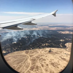 Travel Ad, close-up on a plane flying above a drying landscape, forest fire