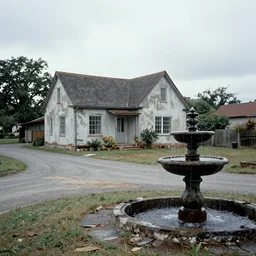 a house in the side of a forgotten road with a dark water fountain