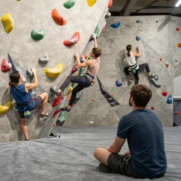 a man is sitting in an airplane, watching his friends enjoy bouldering in a gym. award - winning digital artwork