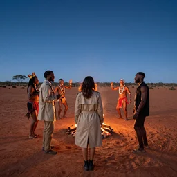 photograph of three ravers, two men, one woman, woman is in a trenchcoat, blessing the soil, seen from behind, talking around a fire, two aboriginal elders, dancefloor kismet, diverse costumes, clean composition, desert transition area, bonfire, starry night, australian desert, xf iq 4, symmetry, sony a 7 r, 1 5 0 mp, 5 0 mm