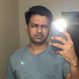 indian dad accidentally taking a selfie with the front facing camera, squinting because the camera flash is so bright