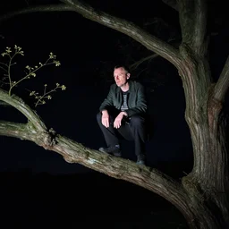 mark e smith perched up on a tree branch at night, flash photography