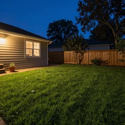 a still photo of a backyard, with grass at night, house on the left side, warm lighting