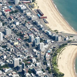 satellite imagery of a small city with shops, shipping dock, and beach to the south. a bridge crosses a big lake, with a town hall, marketplace, and towers to the north. there is a field in the middle of the city. small hills and woods north of the city