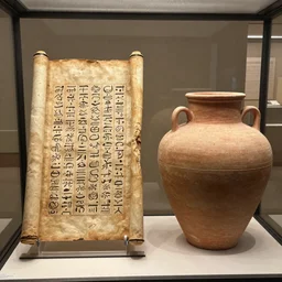 a photo of an ancient scroll with thamudic writing beside a cylindrical clay jar on display in a glass case