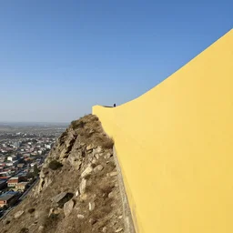 view of a town from mount, the endless cliff on the left, a high yellow wall stretching into the sky on the right