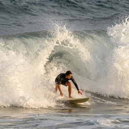 tiny surfer at golden hour, as giant wave is about to crash