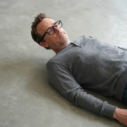 bryan cranston with a black reading glasses while laying on a smooth concrete floor