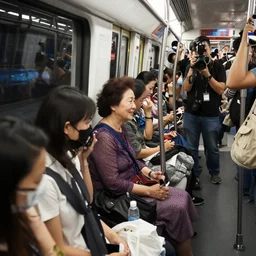 the queen sitting in a crowded singapore mrt train, surrounded by press photographers. reuters photography.