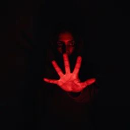 Scary scene of a person coming out of pitch black shadows with hand and eyes illuminated by red light grasping toward the camera, horror, thriller, high contrast, 4k,
