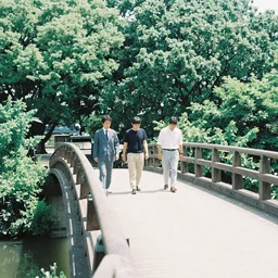 3 japanese men walk on a bridge on the left next to bright greenery on a sunny day, 3 5 mm film, photograph, wide shot, ethereal